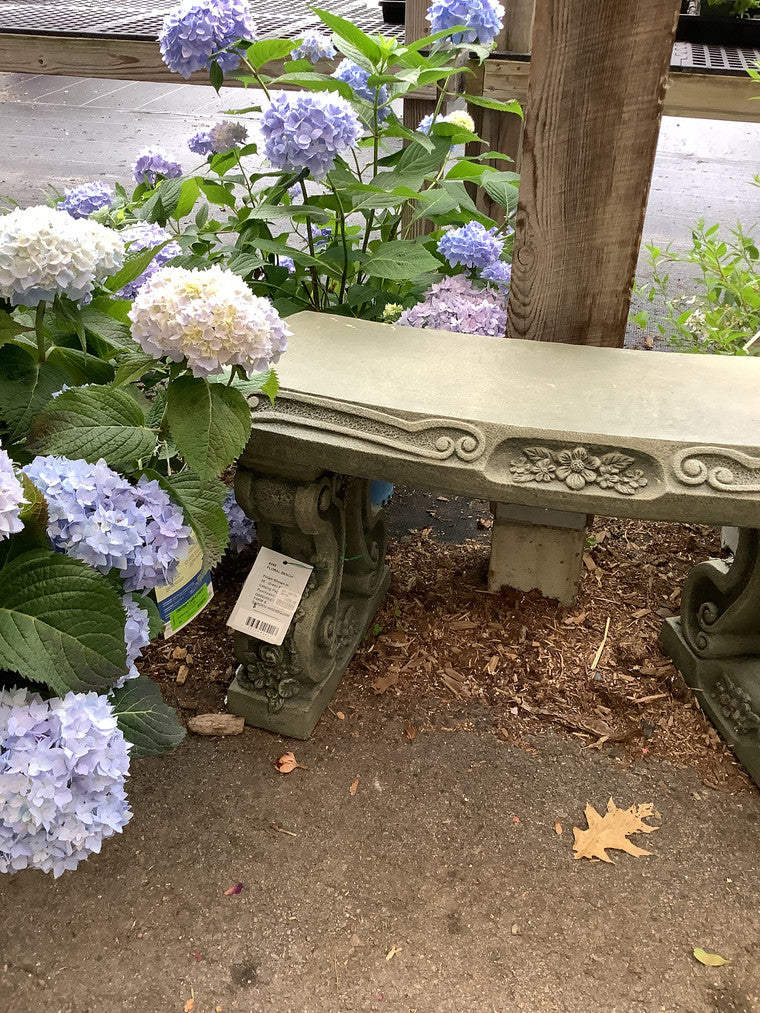 A stone bench adorned with floral accents, with hydrangeas in shades of blue, purple, and white on the left.